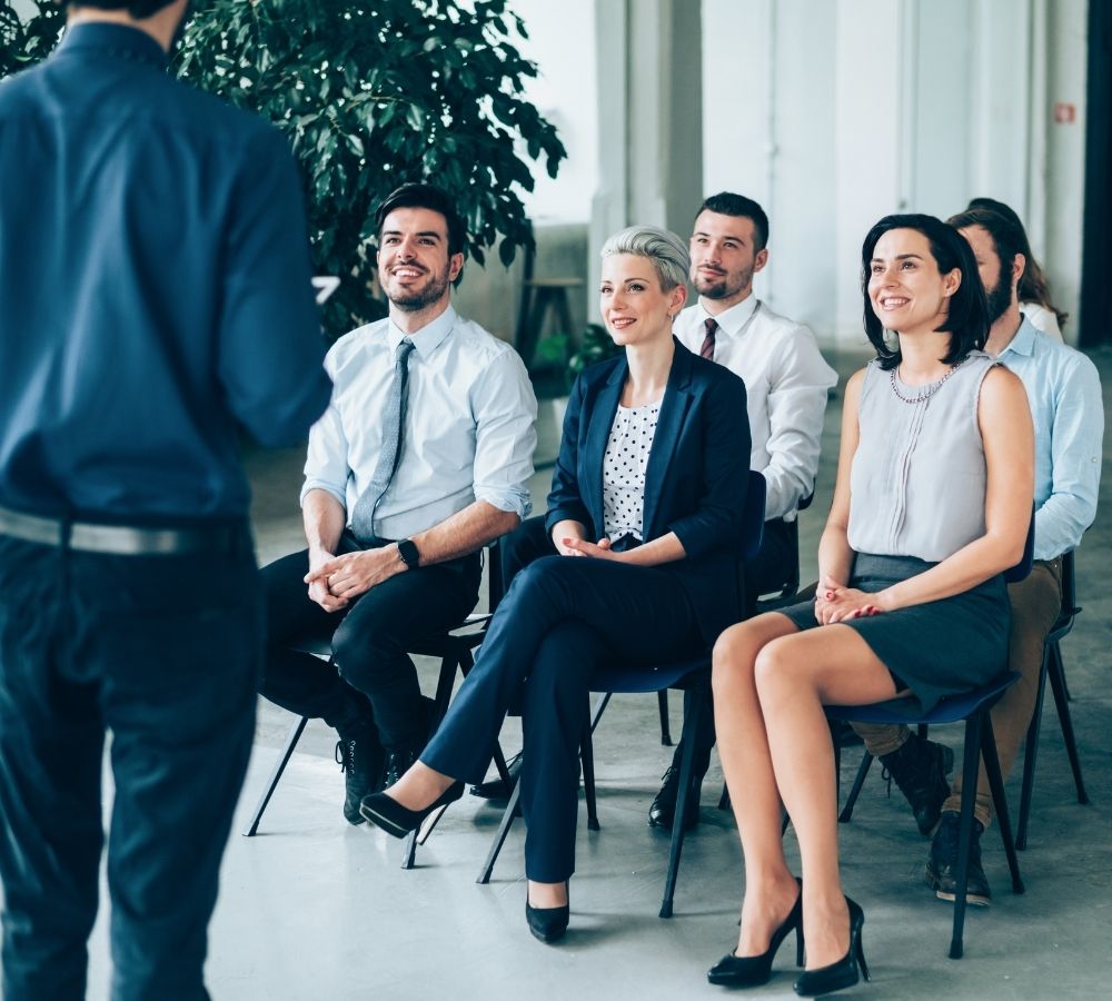 A group of six diverse professionals sit attentively in chairs during a presentation