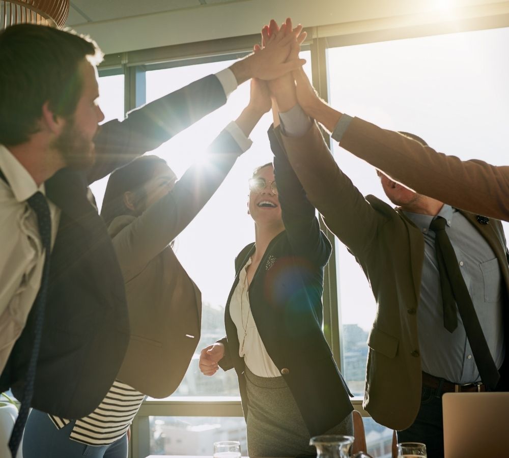 Five business professionals in suits celebrate with a group high-five