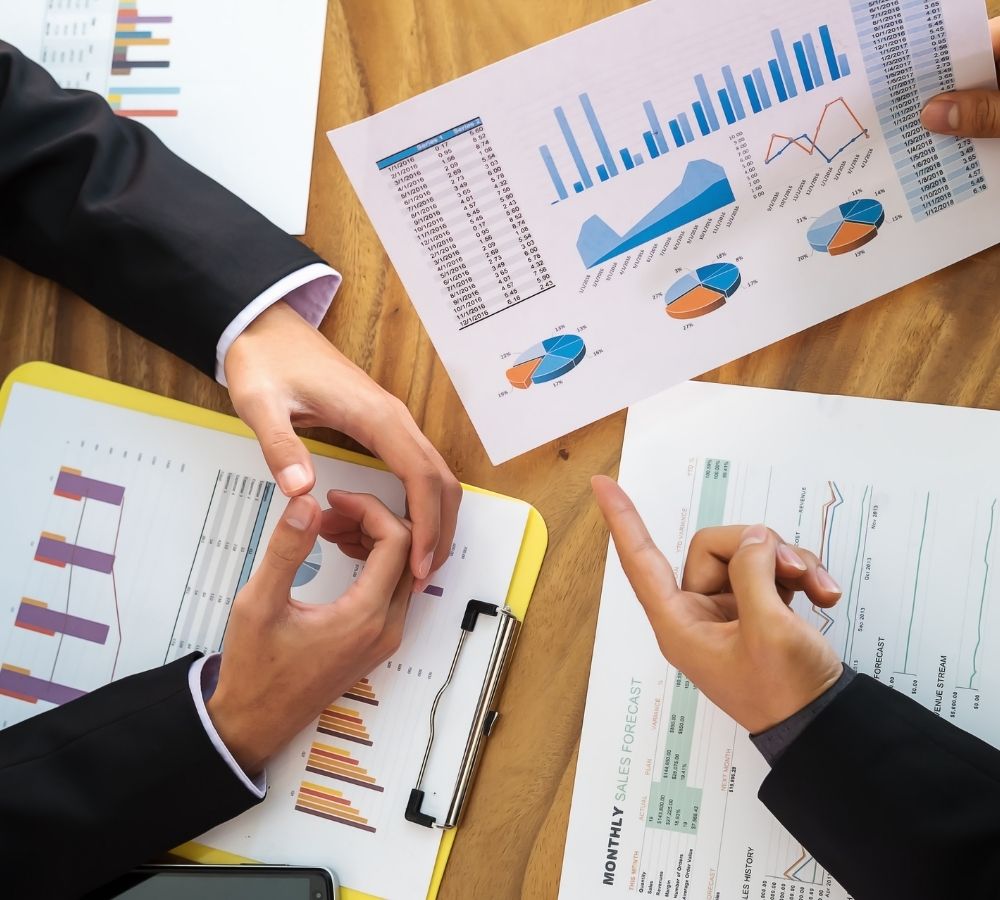 Two people in formal attire discuss colorful charts and graphs on paper, indicating financial data analysis