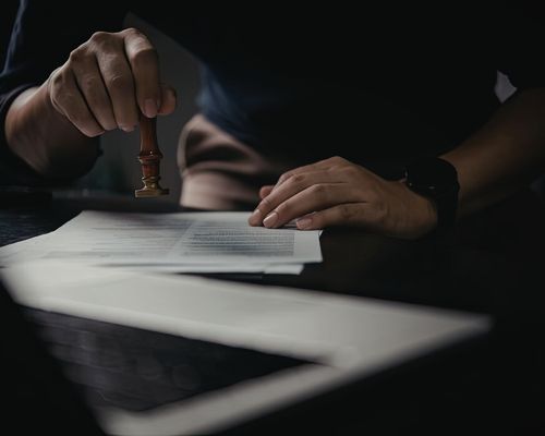 A person stamps a document on a dark desk, suggesting formality and approval