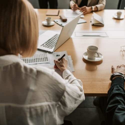 People sitting around a table with laptops, documents, and coffee cups, engaged in a business meeting