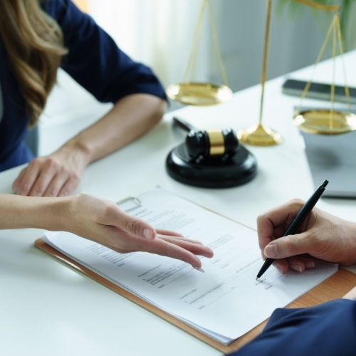 Two people at a desk reviewing a document. One points at the paper while the other signs it