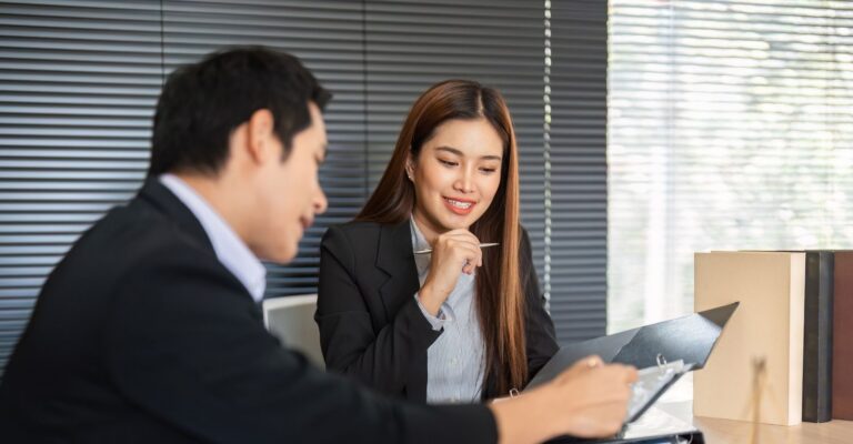 Asian businesswoman and man engaged in a discussion at an office table, reviewing documents and sharing ideas.